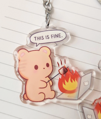 This double-sided funny kawaii keychain features an innocent round brown bear toasting marshmallows over its burning laptop. The front side says, "This is fine," while the back says, "This is not fine," perfectly capturing those chaotic moments we all know too well.