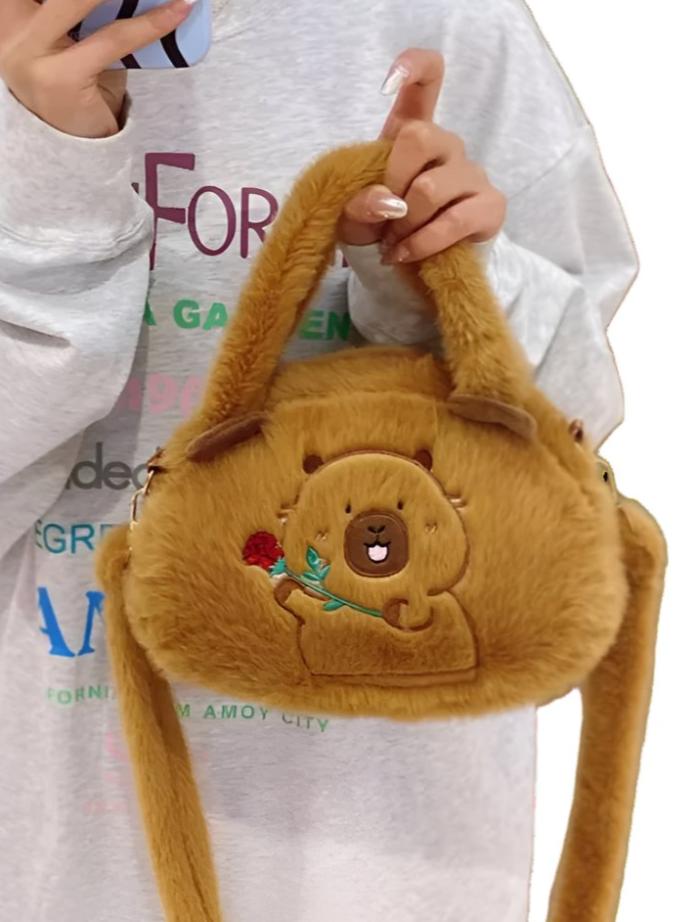 Fluffy Capybara Crossbody Purse! This kawaii bag resembling the body of the beloved capybara will earn you admiring glances wherever you go. The design features an embroidered capybara with a cheerful expression, holding out a flower—purely irresistible cuteness!