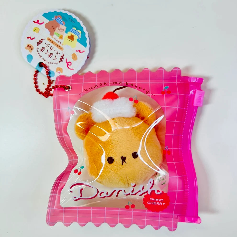 Say hello to the cutest little snack to carry your essentials! This unique Kuma Bakery Bear in a Bag Keychain, Sweet Cherry Danish features a soft, squishy bread bear plushie tucked inside a charming clear and pink mini wallet. The softness is like a mochi dessert and the design is unmatched.